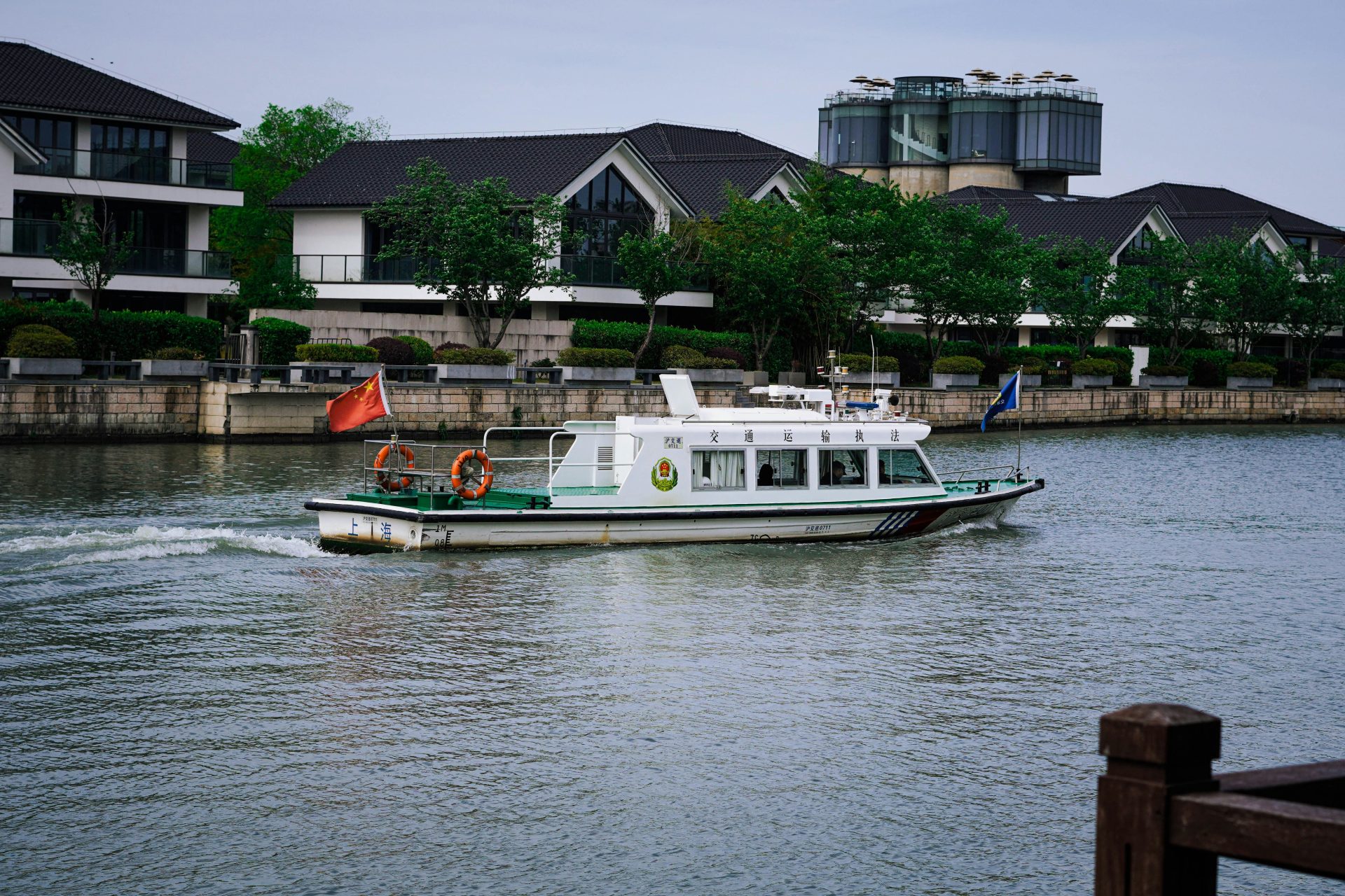Un bateau blanc navigue sur une rivière, longeant des bâtiments modernes.